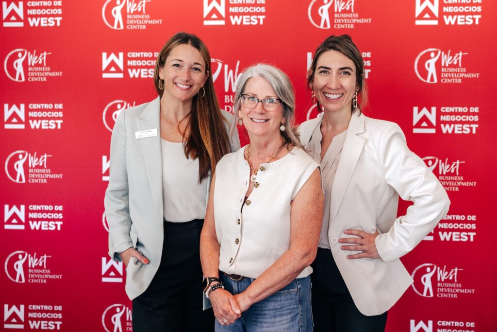 Group standing together posing in front of a red West Business Development Center and Centro de Negocios West backdrop